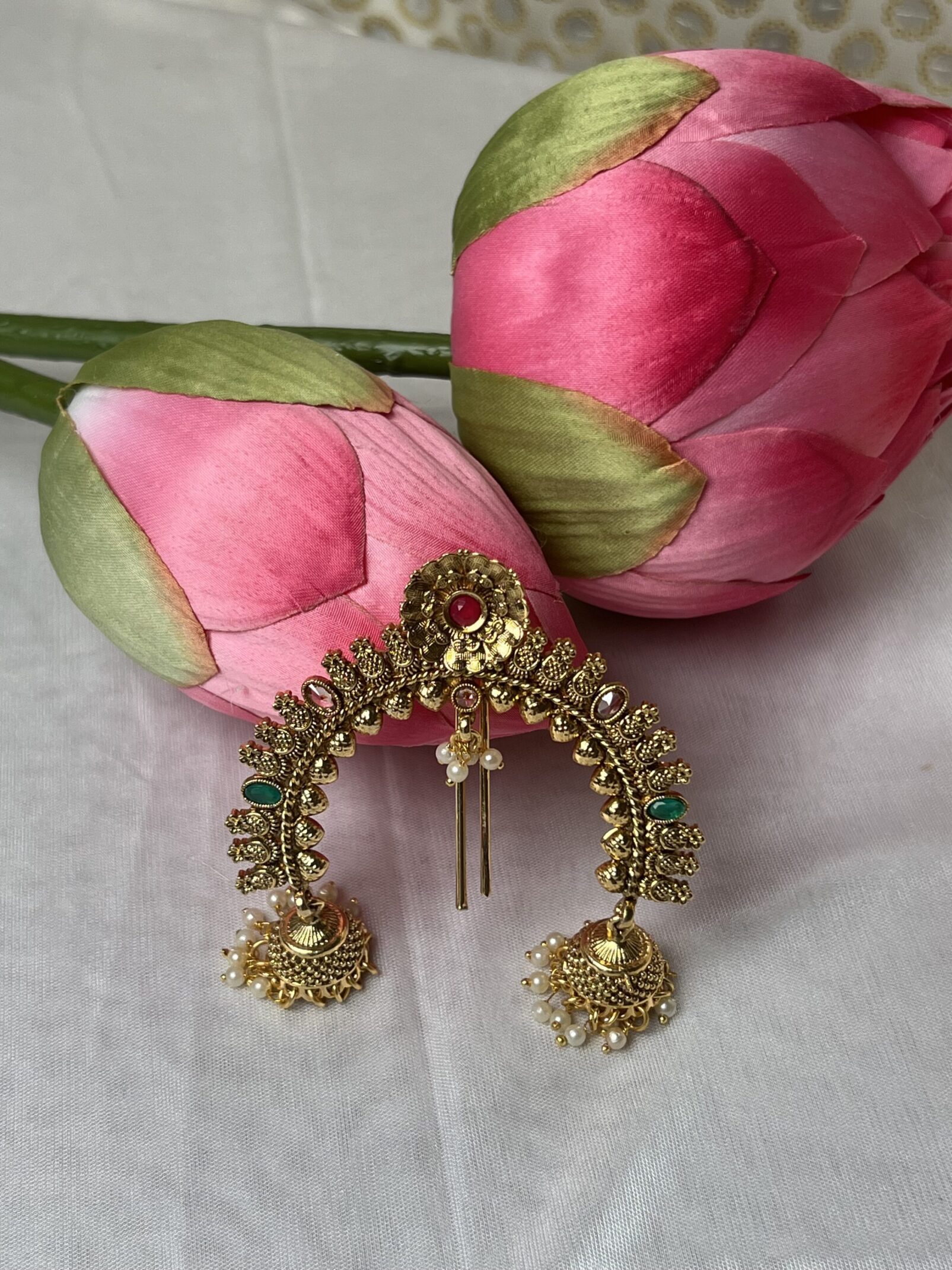 A pair of gold hair ornaments next to pink flowers.