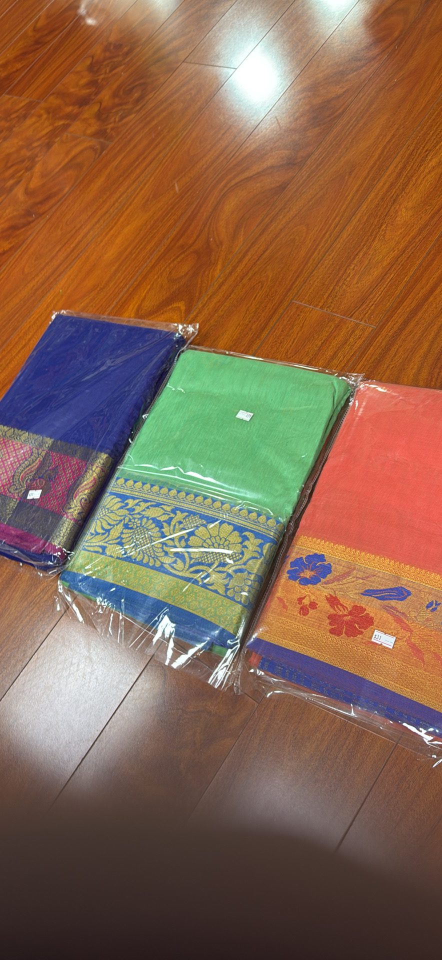 Three different colored sarees on a wooden floor